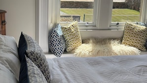 Une chambre avec un grand lit, de nombreux coussins à motifs, un tapis moelleux et une vue sur la plage par la fenêtre.