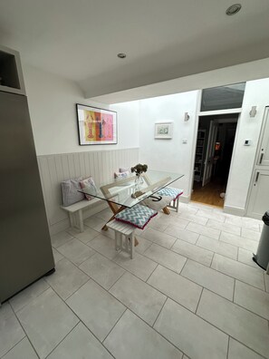 A modern kitchen with a glass dining table, white cabinetry, and a bench with patterned cushions.