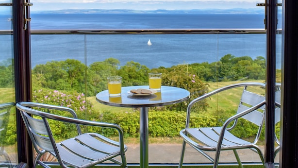 A balcony with a table and two chairs, overlooking a body of water and greenery. - 1 bedroom accommodation in Dippen, near Whiting Bay, Isle of Arran (Dippen, near Whiting Bay, Isle of Arran)