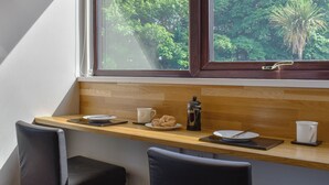 A breakfast setup with a wooden counter, a window with a view of greenery, and a black chair. - 1 bedroom accommodation in Dippen, near Whiting Bay, Isle of Arran (Dippen, near Whiting Bay, Isle of Arran)