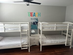 Quarto com beliche, uma pequena mesa de cabeceira com gavetas e um detalhe na parede com a palavra 'BEACH'.
