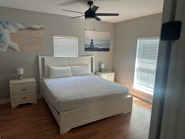 A bedroom with a bed, bedside tables, a ceiling fan, and artwork on the walls. - Blast at the Beach - Golf Cart Available to Rent! Pet Friendly! (Destin)