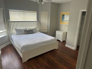 A bedroom with a bed, bedside tables, a nightstand, a ceiling fan, and a window with blinds.