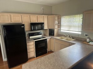 A kitchen with light wooden cabinets, a black refrigerator, a stove, a microwave, and a sink. - Blast at the Beach - Golf Cart Available to Rent! Pet Friendly! (Destin)