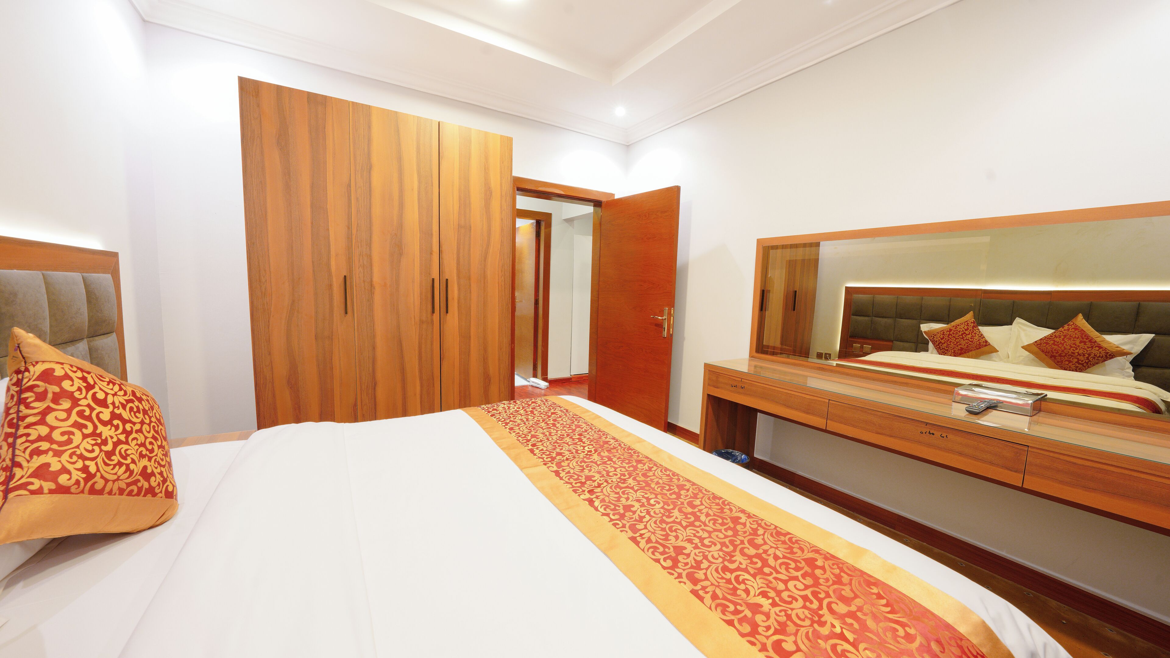 Una habitación de hotel con una cama grande, un armario de madera, un tocador con espejo y una mesita de noche.
