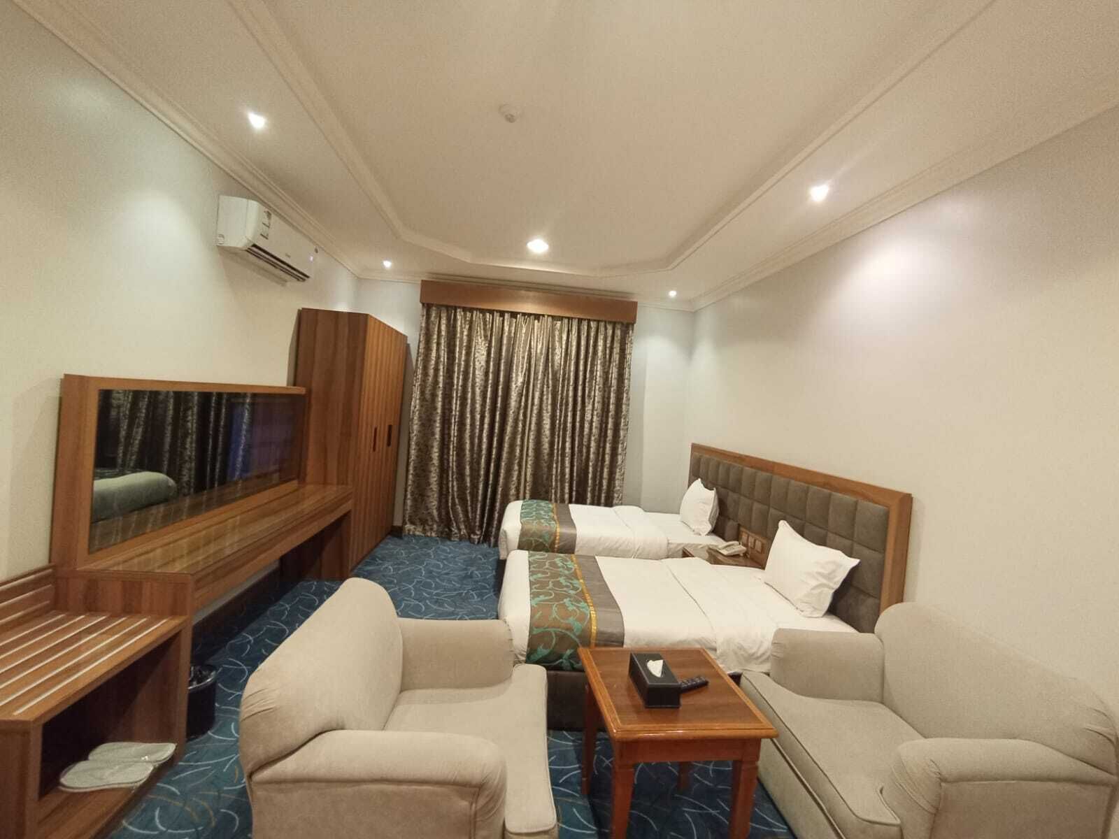 A hotel room with two beds, a TV, a sofa, and a small table.