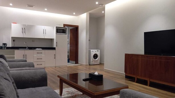 Una sala moderna con un sofá, una mesa de centro, un televisor y una cocina con armarios y electrodomésticos.