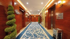 Un pasillo de hotel con paredes de madera, alfombra azul estampada y una planta verde en espiral.