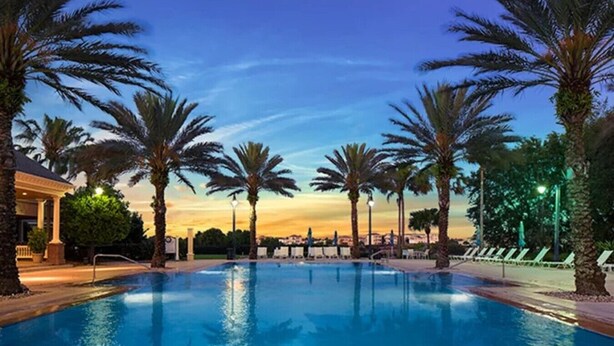 A swimming pool with palm trees and a building in the background. - Fairview at Reunion - Games Room (Kissimmee)