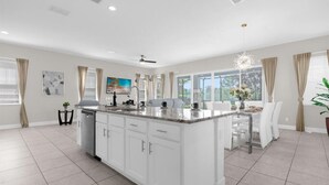 A spacious kitchen with a large island, white cabinetry, and a dining area with a table and chairs. - Fairview at Reunion - Games Room (Kissimmee)