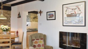 Una sala de estar acogedora con chimenea, un comedor con muebles de madera, y una cocina visible a través de un arco.