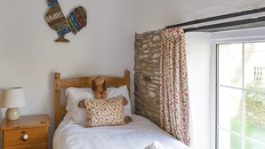 Un dormitorio con una cama de madera, una mesita de noche con lámpara, un gallo decorativo y una ventana con cortinas.