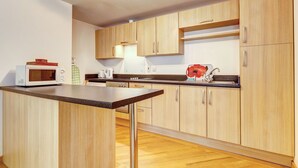 Une cuisine moderne dotée de meubles en bois, d’un four à micro-ondes, d’une bouilloire et d’un évier.