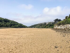 A beach with a clear sky, sandy shore, and houses on a hillside.