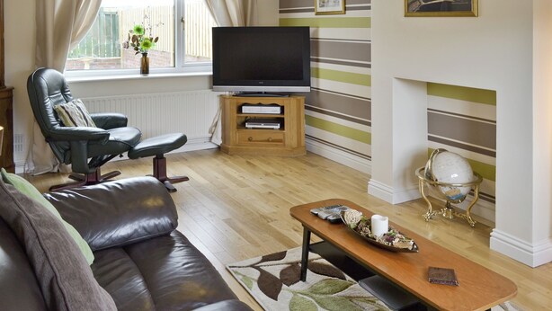 A living room with a leather sofa, a television on a wooden stand, a coffee table with decorative items, and a fireplace with a decorative globe. - Situated close to all the amenities of the fishing port of Whitby. (Whitby)