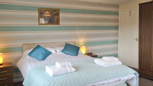 A neatly made bed with pillows, a quilted blanket, and folded towels on a striped wall with a framed picture. - Situated close to all the amenities of the fishing port of Whitby. (Whitby)
