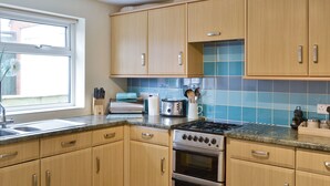 A kitchen with wooden cabinets, a gas stove, an oven, a sink, and a window with a view of the outside. - Situated close to all the amenities of the fishing port of Whitby. (Whitby)