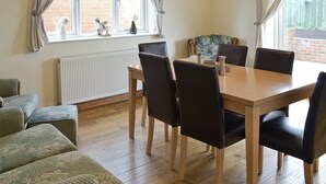 A dining area with a wooden table and black chairs, a radiator, and a window with curtains. - Situated close to all the amenities of the fishing port of Whitby. (Whitby)