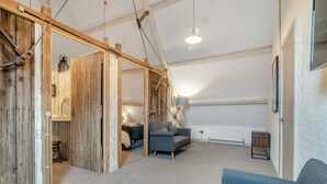 A loft-style room with exposed wooden beams, a sloped ceiling, a grey sofa, a small table, and a radiator. - 5 bedroom accommodation in Huntley (Huntley)