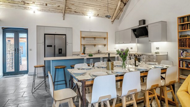 A modern kitchen with a central island, white cabinetry, and a dining area with a table set for six. - 5 bedroom accommodation in Huntley (Huntley)