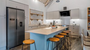 A modern kitchen with a central island, bar stools, stainless steel appliances, and a wooden ceiling. - 5 bedroom accommodation in Huntley (Huntley)