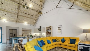 A modern living room with a yellow sectional sofa, a dining area, and a kitchen. - 5 bedroom accommodation in Huntley (Huntley)