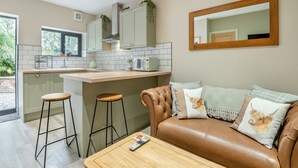 A modern kitchen with a central island, bar stools, a leather sofa with decorative pillows, and a wooden coffee table. - A luxury one bedroom cottage with bubbling hot tub. (South Cerney, near Cirencester)