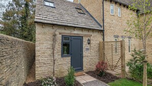 A stone cottage with a dark door, a small window, and a sign reading 'Wisteria Cottage.' - A luxury one bedroom cottage with bubbling hot tub. (South Cerney, near Cirencester)