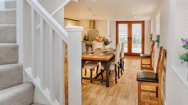 Un interno moderno con una scala, una zona pranzo con tavolo e sedie in legno, e una cucina sullo sfondo.