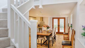 Un interior moderno con una escalera, un área de comedor con una mesa y sillas de madera, y una cocina al fondo.