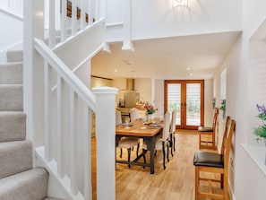 Un interior moderno con una escalera, un área de comedor con una mesa y sillas de madera, y una cocina al fondo.