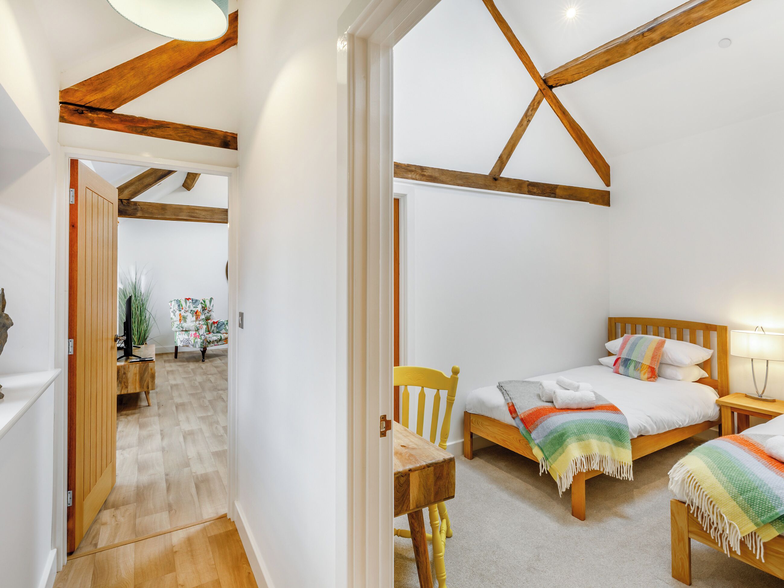 Un dormitorio con dos camas, vigas de madera, una silla y un escritorio.