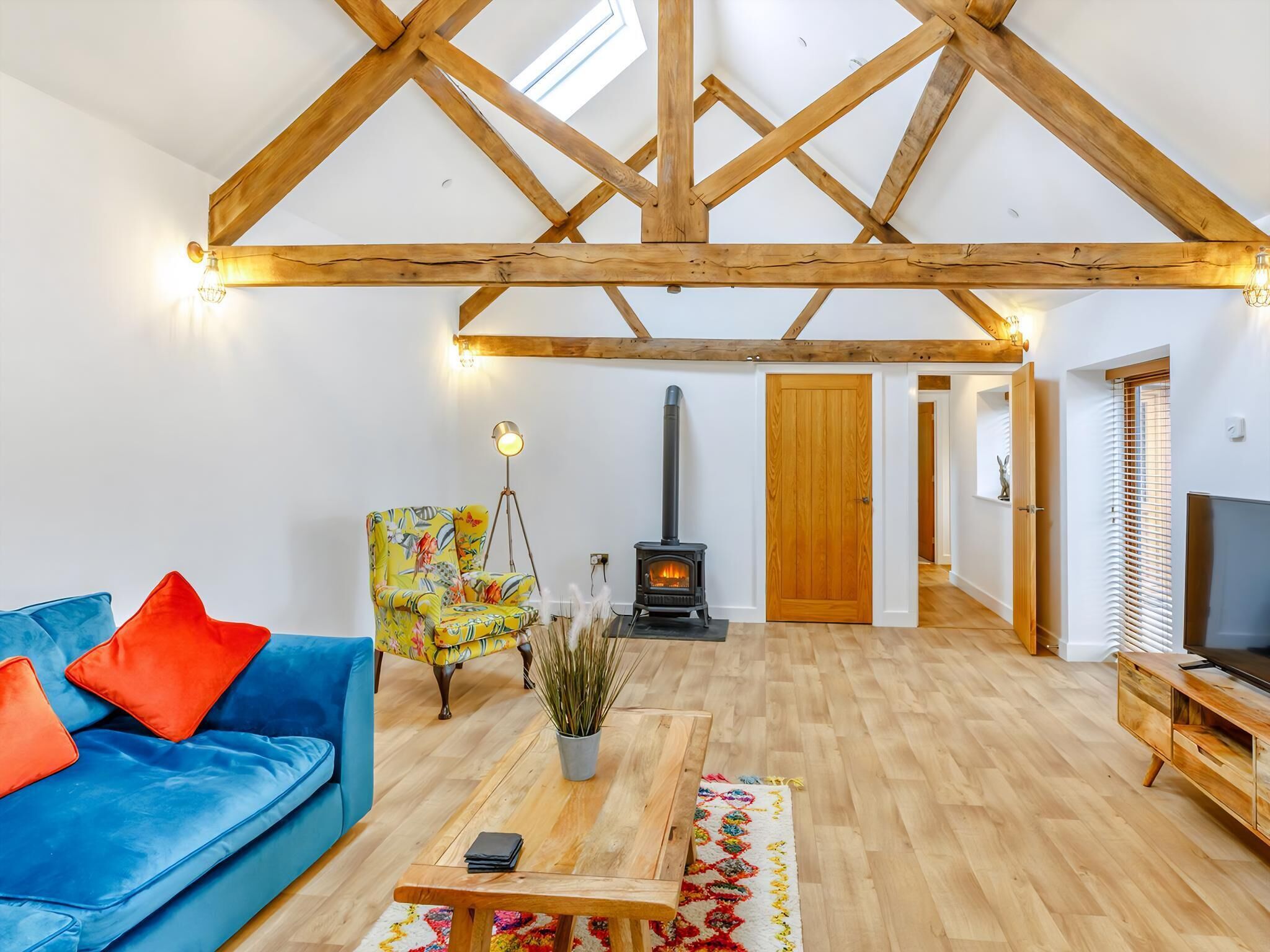 A spacious living room with a high ceiling, a blue sofa, a colorful armchair, a wooden coffee table, a potted plant, and a fireplace.