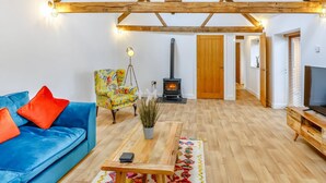 Un ampio soggiorno con soffitto alto, un divano blu, una poltrona colorata, un tavolino in legno, una pianta in vaso e un caminetto.