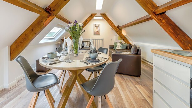 Spisestue på loftet med træloft, et rundt bord og moderne stole.