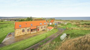 En bygning i sten med rødt tegltag, græsplæne og udsigt over havet.