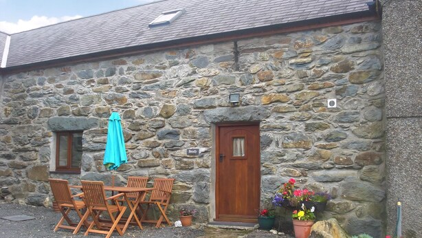 A stone building with a wooden door, a small window, and a table with chairs. - 3 bedroom accommodation in Rhyd Ddu, Caernarfon (Rhyd Ddu, Caernarfon)