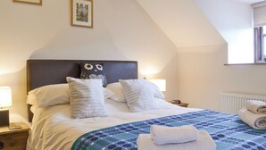 A neatly made bed with a patterned bedspread, pillows, and a folded towel on a wooden nightstand. - 3 bedroom accommodation in Rhyd Ddu, Caernarfon (Rhyd Ddu, Caernarfon)