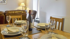 A dining area with a wooden table set for four, including plates, glasses, and cutlery. There is a bottle of wine and a lamp in the background. - 3 bedroom accommodation in Rhyd Ddu, Caernarfon (Rhyd Ddu, Caernarfon)