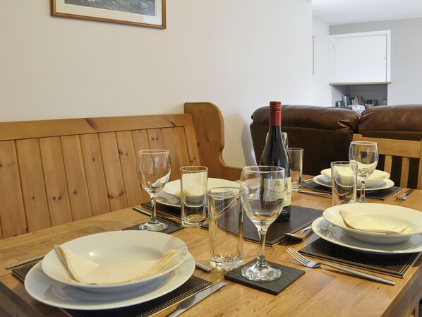 A dining table set with plates, glasses, and a wine bottle, surrounded by wooden furniture and a brown leather couch.