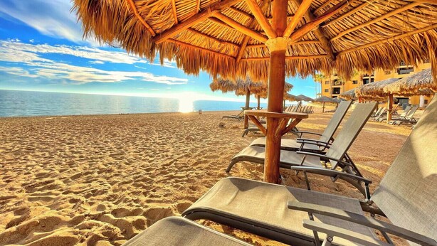 Una spiaggia con ombrelloni di paglia e lettini, cielo sereno e l'oceano sullo sfondo.