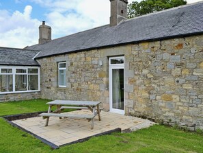 A stone building with a tiled patio, a wooden table, and a door. - 3 bedroom accommodation in Belford, near Bamburgh (Belford, near Bamburgh)