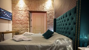 Habitación de hotel con pared de piedra, cama con cabecera verde, televisor de pantalla plana y escritorio de madera.