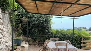 An outdoor patio with a table and chairs, surrounded by potted plants and a view of the sea. - Small house on a hill, quiet with sea view, sunny terrace (Menton)