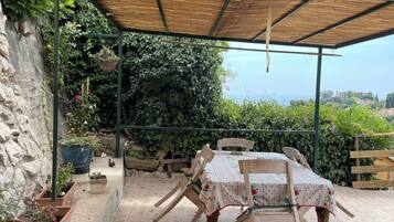An outdoor patio with a table and chairs, surrounded by potted plants and a view of the sea.