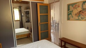 A bedroom with a bed, a wooden bench, a wardrobe, and a door leading to another room. - Small house on a hill, quiet with sea view, sunny terrace (Menton)