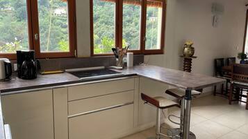 A kitchen with a central island, wooden cabinets, a coffee maker, and a view of greenery through large windows.