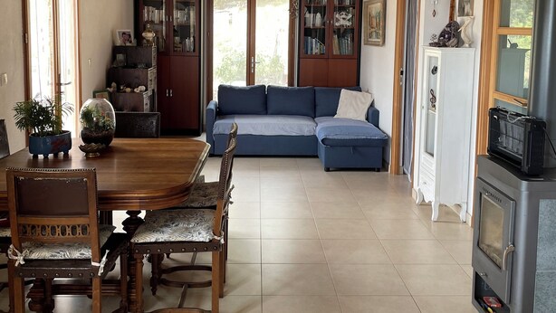 A spacious living area with a wooden ceiling, a blue sofa, a dining table with chairs, and a kitchen area with a stove. - Small house on a hill, quiet with sea view, sunny terrace (Menton)