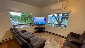 A living room with a large flat-screen TV, a dark brown leather sofa, and a patterned rug. - House in Harrison with Lake View (Harrison)
