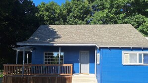 A single-story house with a blue exterior, a front porch with a wooden railing, and a grey roof. - House in Harrison with Lake View (Harrison)